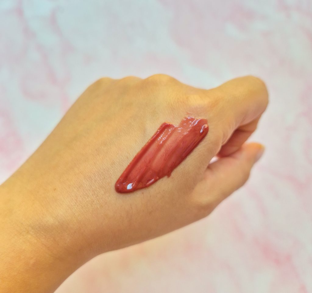 Texture lucida rosa-bruno del trattamento labbra ai peptidi Essence nella tonalità 06, stesa sul dorso della mano.